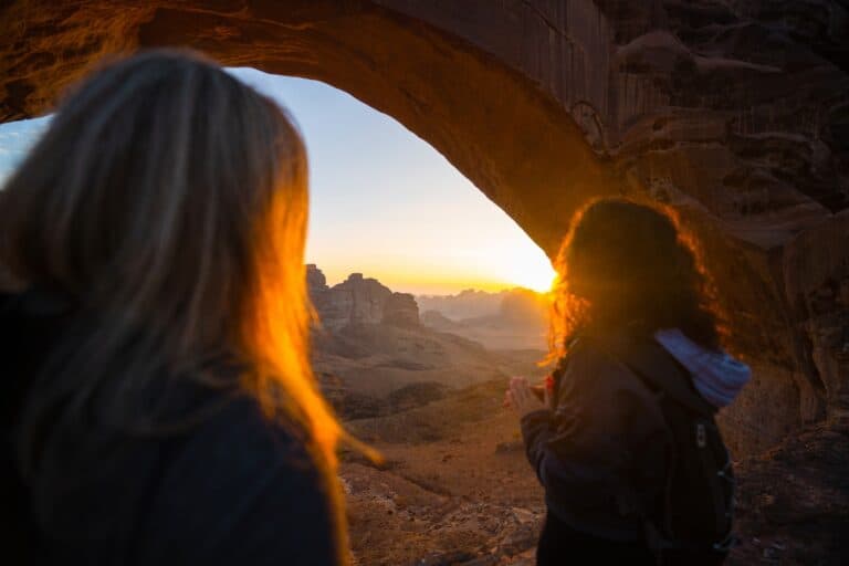 A tranquil scene of two women overlooking a desert landscape at sunset from within a natural rock arch, symbolizing hope and new beginnings in drug detox and rehabilitation journeys.