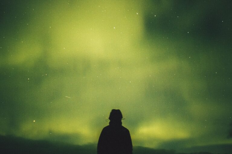 Bright northern lights illuminating night sky with silhouette of a person looking up. Beautiful natural aurora borealis over a calm landscape, emphasizing hope and recovery in drug detox and rehab.